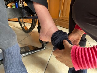 person putting on socks for the man in wheelchair