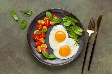Fried eggs and Caprese salad with tomatoes, mozzarella cheese and basil leaves in a plate. Top view.
