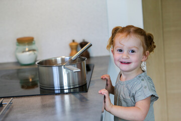 Smiling little girl in a kitchen with a pan on hob