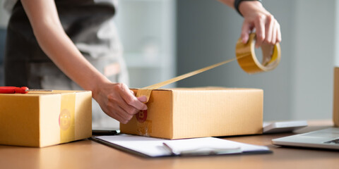 Woman use scotch tape to attach parcel box to prepare goods for the process of packaging, shipping, online sale internet marketing ecommerce concept startup business idea