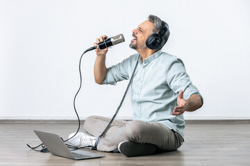 Man learning how to sing by using laptop, mic and headphones in his living loom.