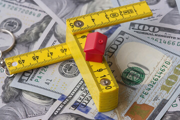 A centimeter ruler and a model house displayed against a background of one hundred dollar bills,...