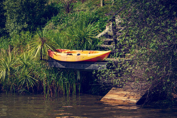 Bright yellow kayak drying on a private jetty hidden in the lush green at the bottom of a steep hill. Retro style