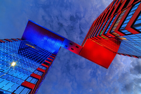 Modern glass illuminated building (business center with offices) against cloudy dramatic sky in Novosibirsk city (Russia) at night.