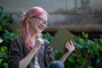 Cute pink hair girl drawing on digital tablet in garden, Woman Doing Freelance Work in Garden,...