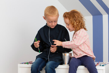 Two young children a girl and a boy having fun with paintbrushes