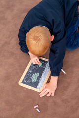 Little blond boy drawing with a chalk slate