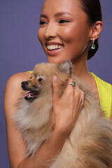 Close up portrait of a beautiful elegant asia woman and spitz dog with stylish jewelry on a blue background. Asian cute girl in stylish dress. Beautiful girl with jewelry.