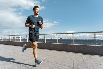 Athletic man running on a waterfront promenade with a clear sky, personifying dedication and a healthy, active lifestyle.