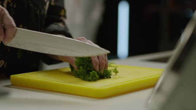 Female Hands Cut Greens With A Knife In The Kitchen On A Cutting Board