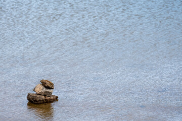 Stone cairn on striped on the water, three stones tower, simple poise stones, simplicity harmony and balance, rock zen sculptures. Horizontal