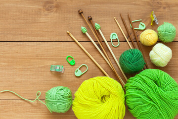 Top view of accessories and supplies for needlework and hand knitting: set of green and yellow wool yarn, knitting needles and crochet hooks on wooden table. Flat lay, copy space, close-up, mock up