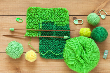 Close-up view of hand knitting square pattern using 10-stitch method from wool yarn in different shades of green color on wooden table. Spring crafts and needlework. DIY concept. Flat lay, top view