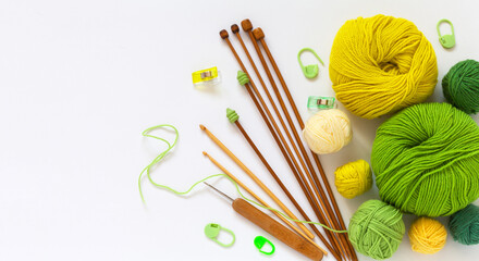 Flat lay of accessories for needlework and hand knitting: set of green and yellow wool yarn, knitting needles, crochet hooks on white background. Empty space for text, blank, top view, mock up