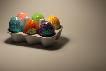 Colorful and sparkling artificial ester eggs in a white porcelain egg box. White background plenty of space for text.