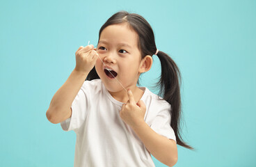 Korean sweet little girl cleaning his teeth with a dental floss on blue isolated. 