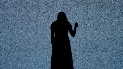 Silhouette against digital television screen. Thriller scene scared woman with knife walks back in front of big digital screen with white noise.