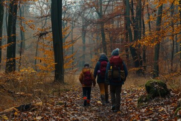 Fototapeta premium Back view of a family with backpacks hiking through an autumnal forest on a trail.
