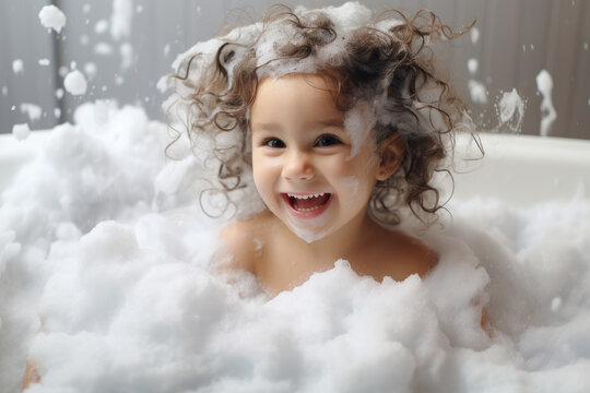 Happy little girl bathes in a bathtub white foam on her face