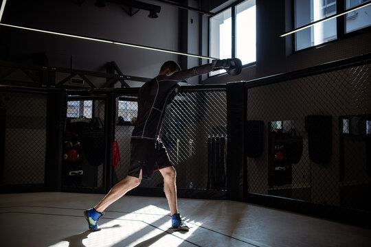 Male athlete shadowboxing in well equipped MMA cage