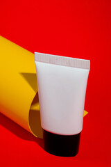 Cosmetic product in tube, bottle, lotion or serum on yellow and red background.