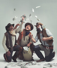 Money, thief and western with celebration of people in studio on gray background for robbery or heist. Texas, crime and smile with man gang throwing cash from bag in air for illegal theft or stealing - obrazy, fototapety, plakaty