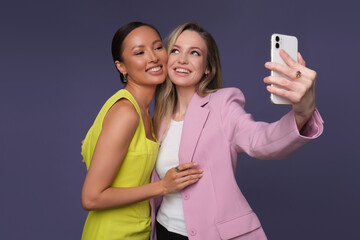 two beautiful girls, an Asian and a European, photograph themselves in beautiful jewelry on a blue background. cute girls dressed in stylish dresses