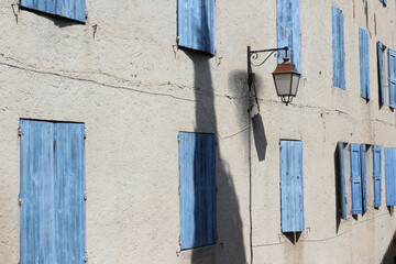 Lateral and close up shot of half closed blue shutters on a stone facade in Beaucaire, Provence, Gard.