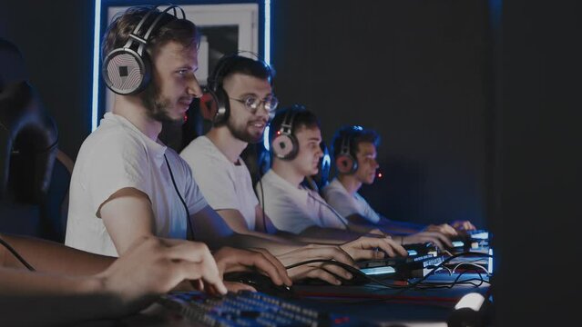 Gamers of team puts on headsets at PC computer club, cyber sport tournament. E-sport championship. 5 players in headphones playing video game. Multiplayer online battle, tactical first-person shooter