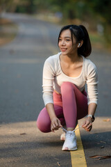 Focused young woman tying her running shoe, preparing for a jog.