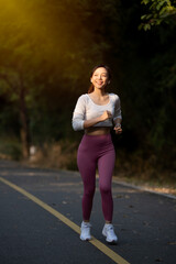 Cheerful woman enjoys jogging on the street in the warm morning sun.