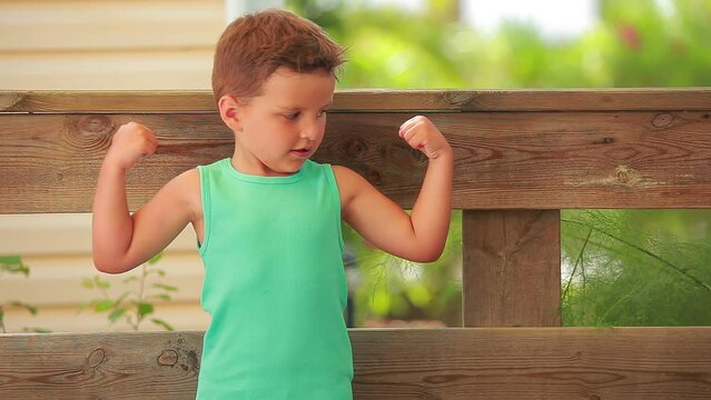 A boy in a green T-shirt funny shows his muscles on a sunny day. High quality 4k footage