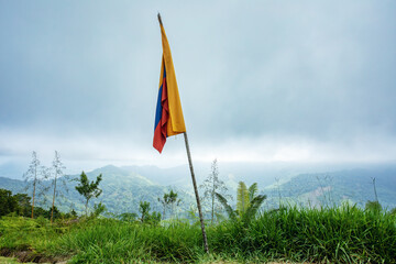 Misty and fogy landscape with colombian flag on high peak. Trek to hidden ancient ruins of Ciudad Perdida in Colombian jungle. Santa Marta, Sierra Nevada mountains, Colombia wilderness. - 743734047