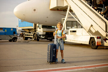Cute blond child, kid with backpack, boarding airplane at the airport on sunset, enjoying the view