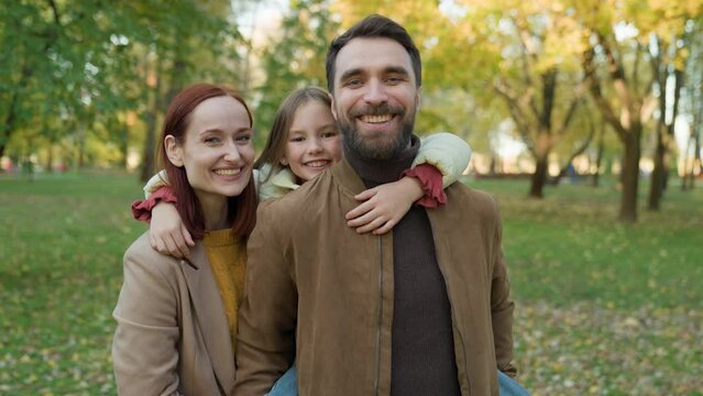 Happy Caucasian smiling family portrait in city outdoors together smile laughing parents with little daughter piggyback hold dad in autumn fall park mother father with child kid girl piggy back game