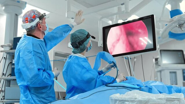 A team of doctors performs a laparoscopic surgery in the operating room while monitoring the procedure on a screen.
