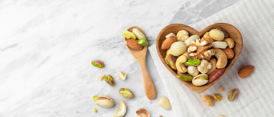 Nuts mixed in heart wood bowl on marble table background with linen cloth, top view