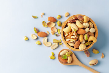 Nuts mixed in wooden bowl with spoon on blue background, top view