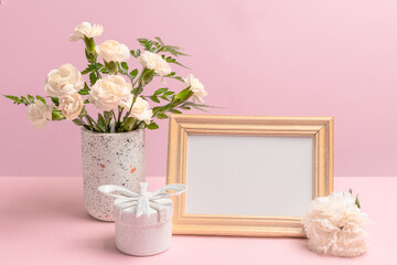 Bouquet of carnations in a vase with a gift box and a photo frame.