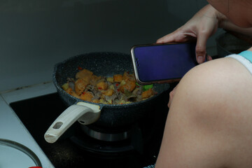 an Asian woman takes a photo of her cooking with her smartphone