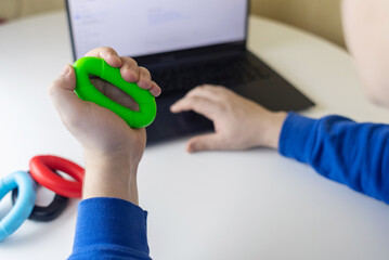 Hand gripper. Man squeezes rubber expander while working on his laptop. Concept of combining useful activity with necessary work. Training hand and arm muscles. Multi-colored mini training apparatus