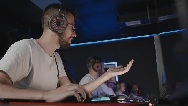 Bristly adult gamer in headset playing PC video game at computer club with team cyber sport tournament. E-sport championship. 5 player in headphones. Multiplayer online real-time strategy shooter