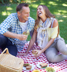Love, laughing and picnic with couple in park together, drinking wine for celebration, romance or bonding. Food, smile or funny with happy mature man and woman on grass for anniversary in summer