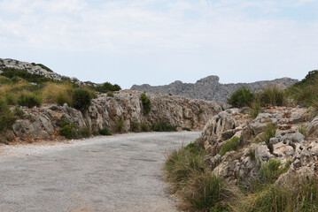 Path in the mountains. View of the mountain road. Serpentine on the mountain between rocks and greenery. Sunny weather with a blue sky. Alcudia, Majorca. 