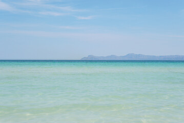 Fototapeta na wymiar A gorgeous beach with super clear, turquoise water. Mountains in the distance. Sunny weather with a bright blue sky. Alcudia, Majorca. 