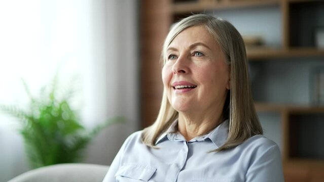 Senior female relaxing with her eyes closed while sitting in the living room. Portrait of a calm happy elderly woman resting breathing deeply on comfortable couch at home. Meditation concept. Close up