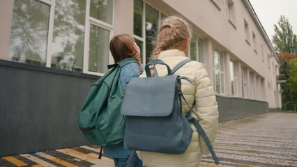 Back view two little girls girlfriends walk street city outside stroll friendship learners schoolgirls sisters laughing togetherness chatting conversation humorous playful kids joy carefree funny move