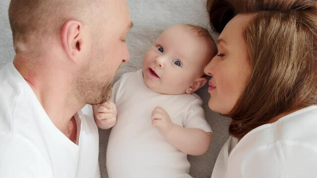 Happy parents kissing his newborn baby with, top view. Happy family.  Healthy newborn baby with mom and dad. Close up Faces of the mother, father and infant baby.  Cute  Infant boy and parents.