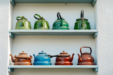 Vintage teapots in various colors and finishes are neatly arranged on a blue shelf. The collection...