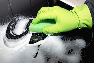 A man wearing cleaning gloves wipes the induction hob.